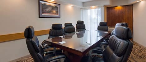 Un salón de conferencias con una larga mesa, sillas de cuero negro y un cuadro en la pared.