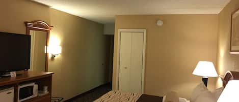 Habitación de hotel con cama, televisor en cómoda de madera, microondas, lámpara y puerta.