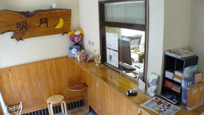 Una pequeña recepción con un mostrador y un taburete de madera, una ventana pequeña y un cartel con caracteres japoneses colgado en la pared.