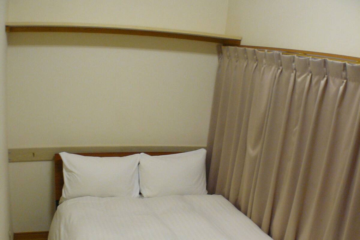 A neatly made bed with white linens, a folded white towel, and a wooden headboard.