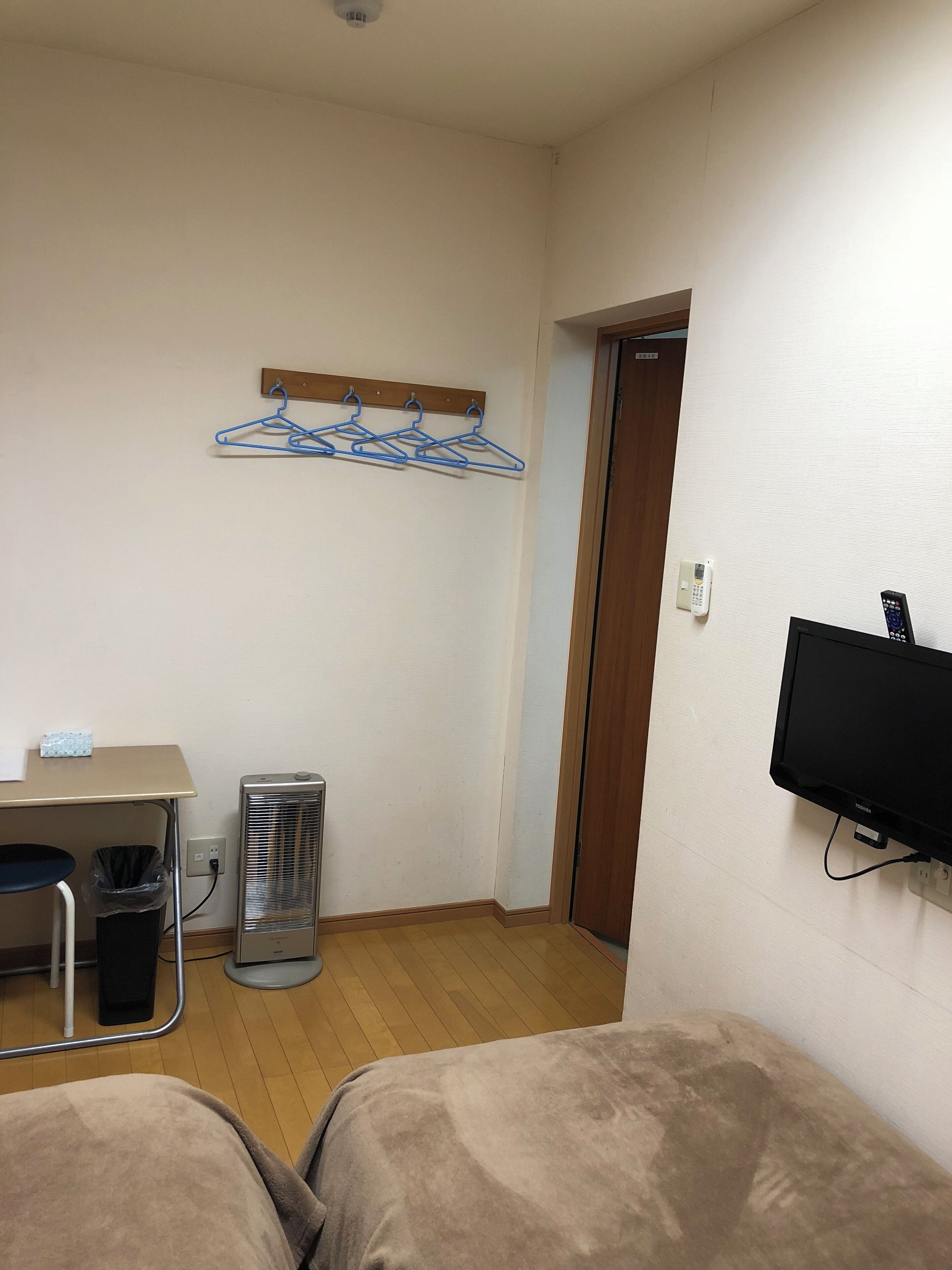A small room with two beds, a desk, a chair, a heater, a TV, and a clothes drying rack.