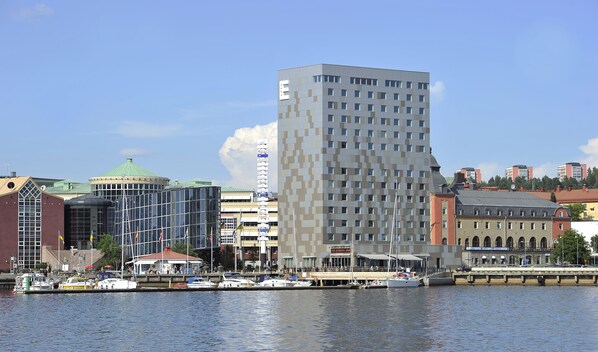 Un hotel moderno con una fachada geométrica distintiva, ubicación frente al agua y vistas del horizonte urbano.