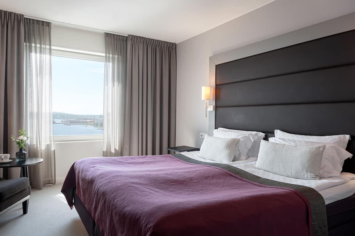 A hotel room with a large bed, a nightstand, a desk, and a view of the water.