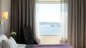 A hotel room with a bed, a chair, a lamp, and a view of a body of water through the window. - Elite Plaza Hotel, Örnsköldsvik (Ornskoldsvik)