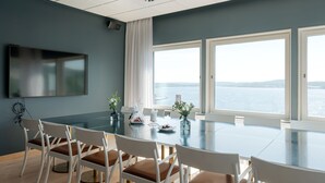 A conference room with a large table, white chairs, a flat-screen TV, and a view of the sea. - Elite Plaza Hotel, Örnsköldsvik (Ornskoldsvik)