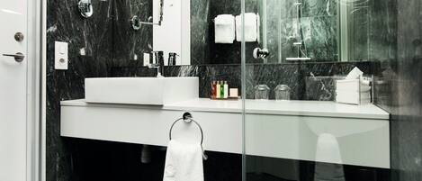 A modern bathroom with a white sink, a glass shower enclosure, and a marble backsplash.