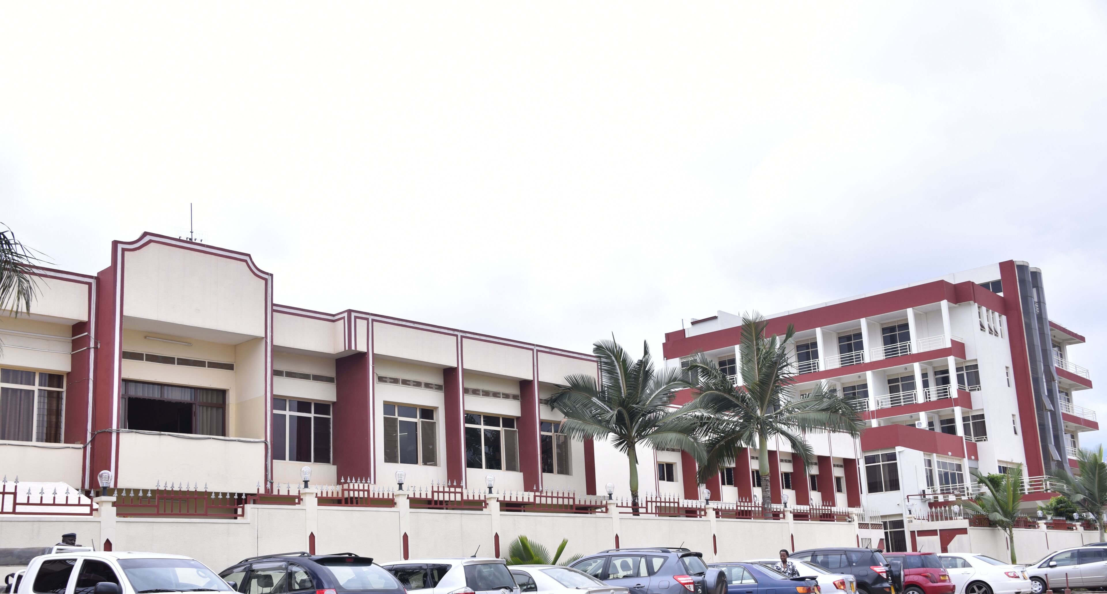 A multi-story building with a symmetrical facade, large windows, and a parking lot with several cars.