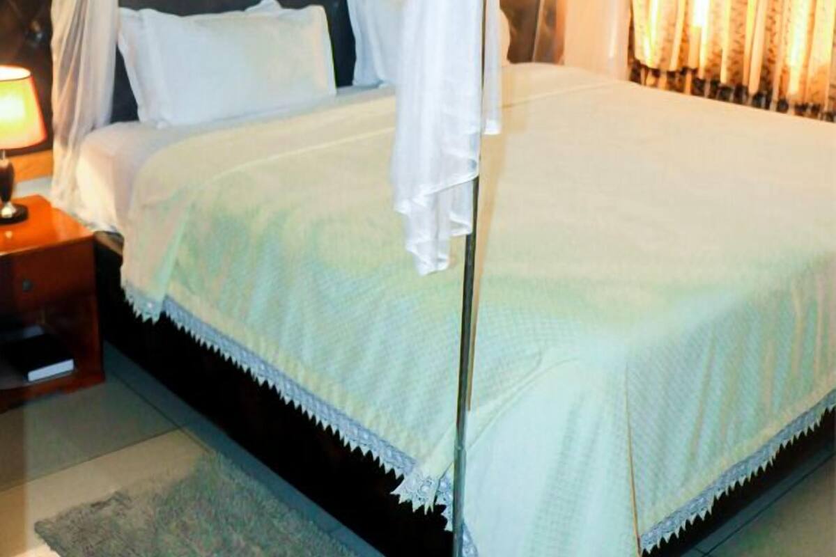 Un lit à baldaquin à quatre poteaux, doté d’une tête de lit capitonnée, de linge de lit blanc et d’une table de chevet avec une lampe.