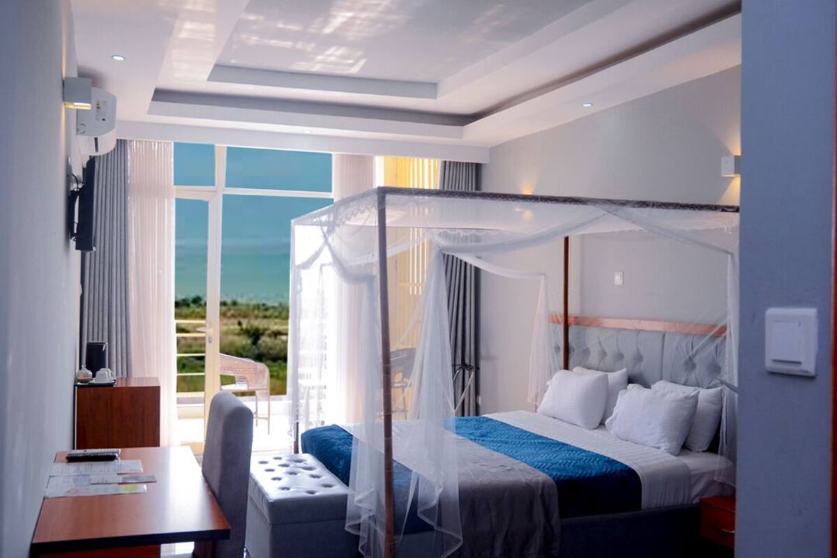 Une chambre d’hôtel avec un lit à baldaquin, un bureau avec une chaise et une vue sur l’extérieur grâce à de grandes fenêtres.