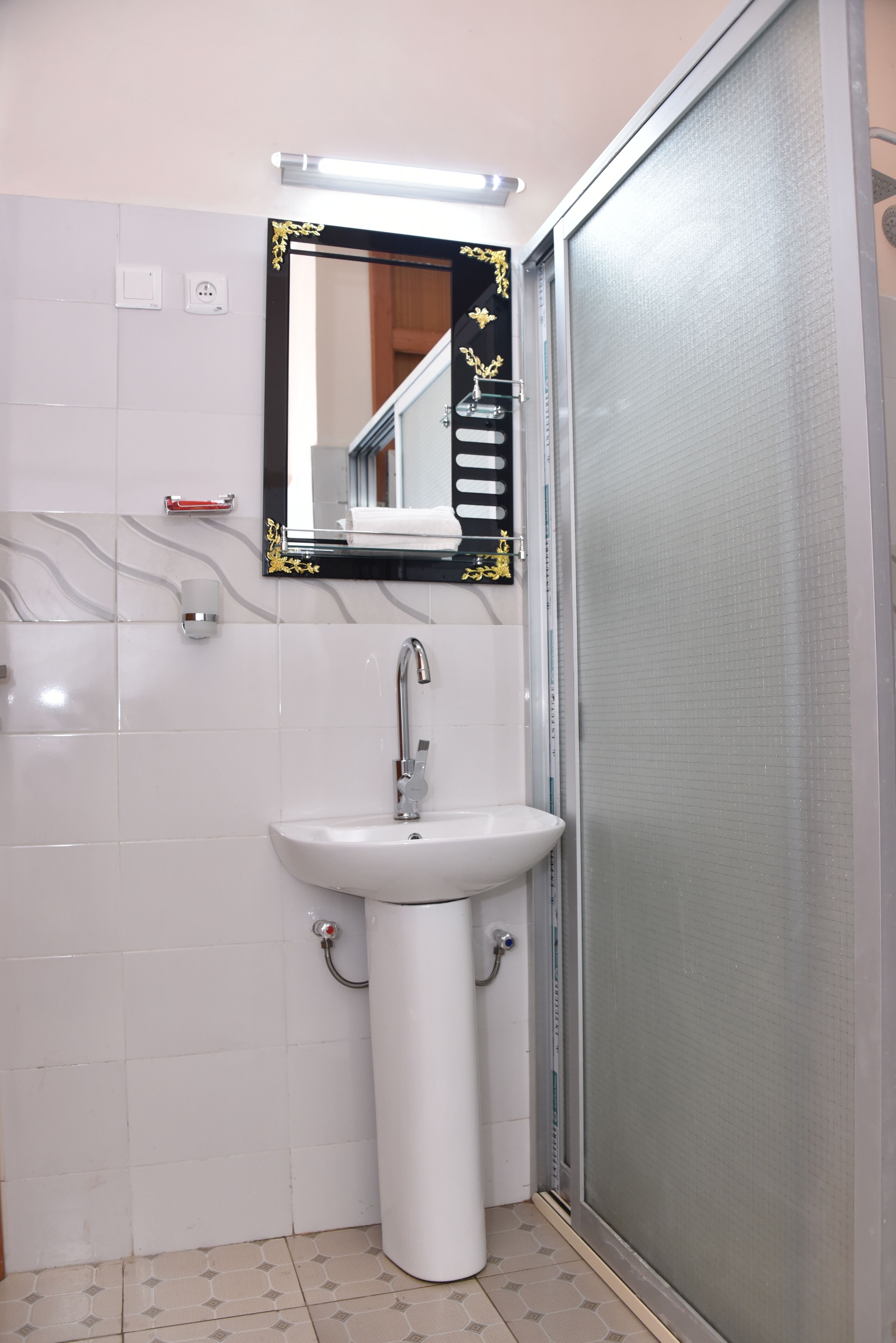A bathroom with a white sink, a mirror with a gold frame, and a shower enclosure.