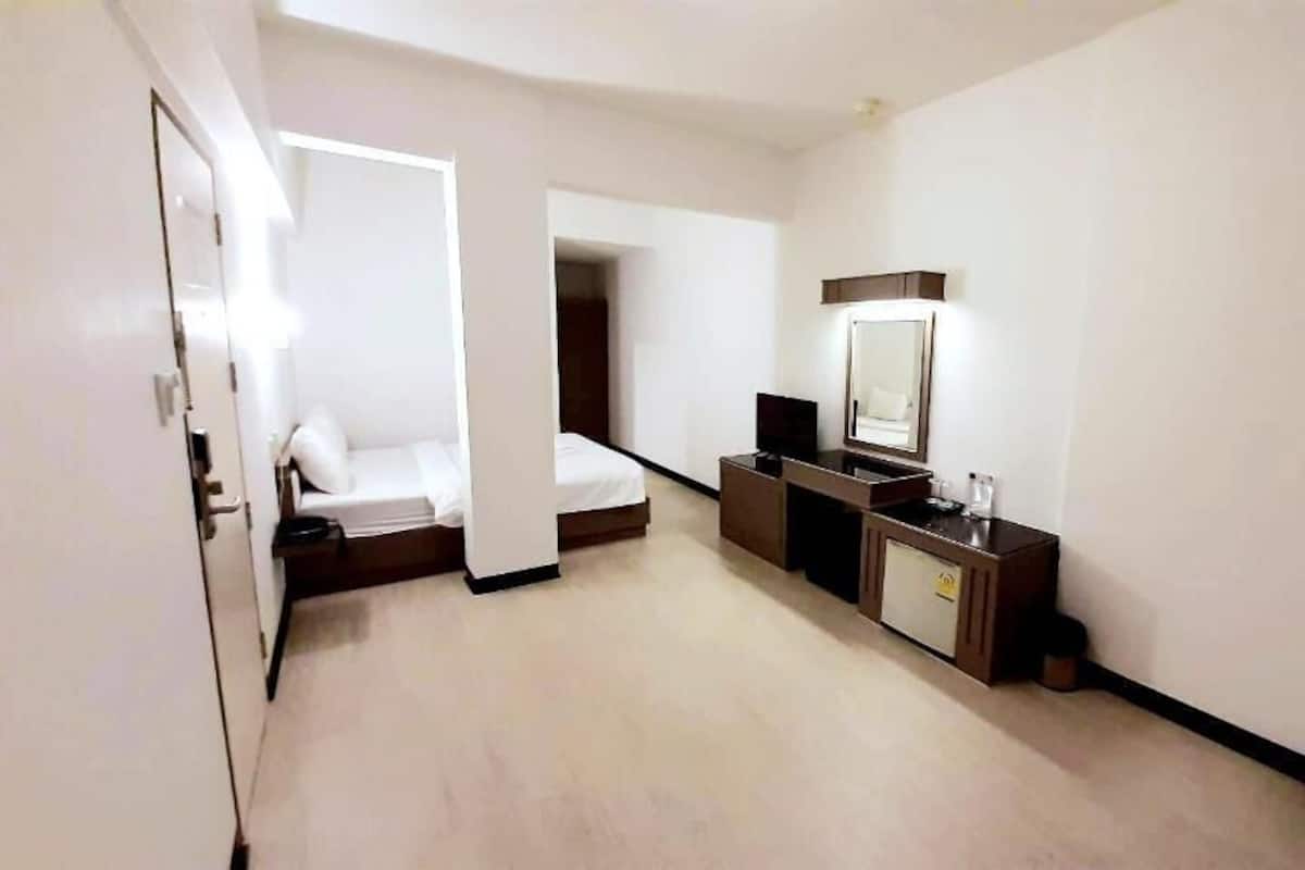 A hotel room with a bed, a desk with a mirror, a television, and a small cabinet.