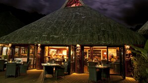Een restaurant met rieten dak, terras en uitzicht op de bergen in de nacht.