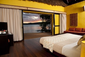 Une chambre avec un lit, une télévision et une vue sur un lac au coucher du soleil.