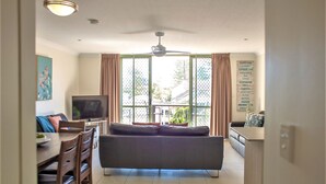 Una sala de estar con sofá, televisor, mesa de comedor, sillas y ventilador de techo.