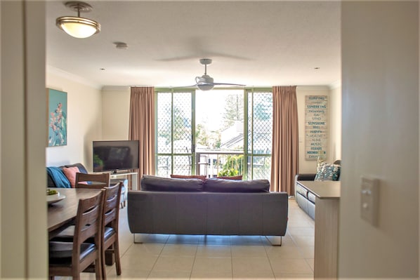 A living room with a sofa, TV, dining table, chairs, and a ceiling fan.