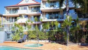 Un hotel de varios pisos con balcones, piscina y jardines tropicales.