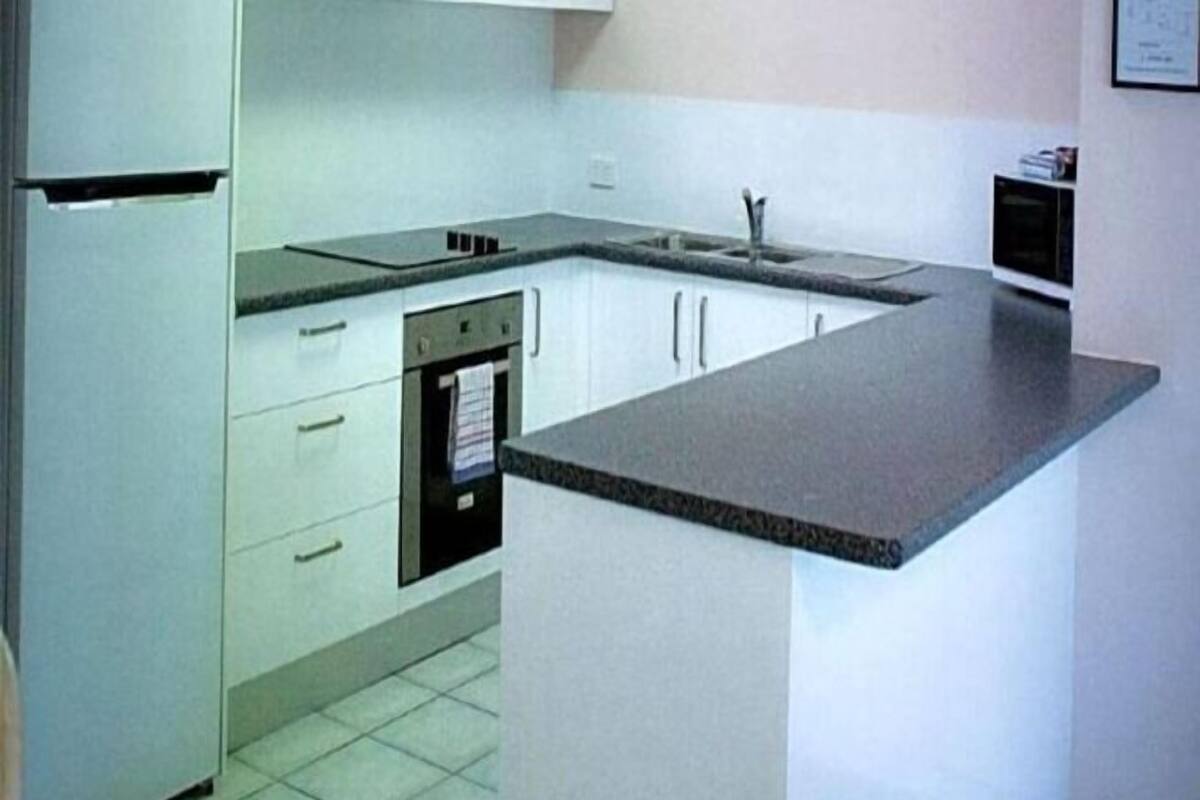 Eine Küche mit weißen Schränken, einer schwarzen Arbeitsplatte, einem eingebauten Backofen und einer Mikrowelle.