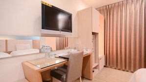 Una habitación de hotel con cama, escritorio, silla, televisor y ventana con cortinas.