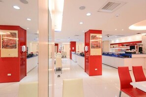 A modern hotel lobby with red accents, a central reception desk, and a dining area with white chairs. - i-Deal Hotel (Taichung)
