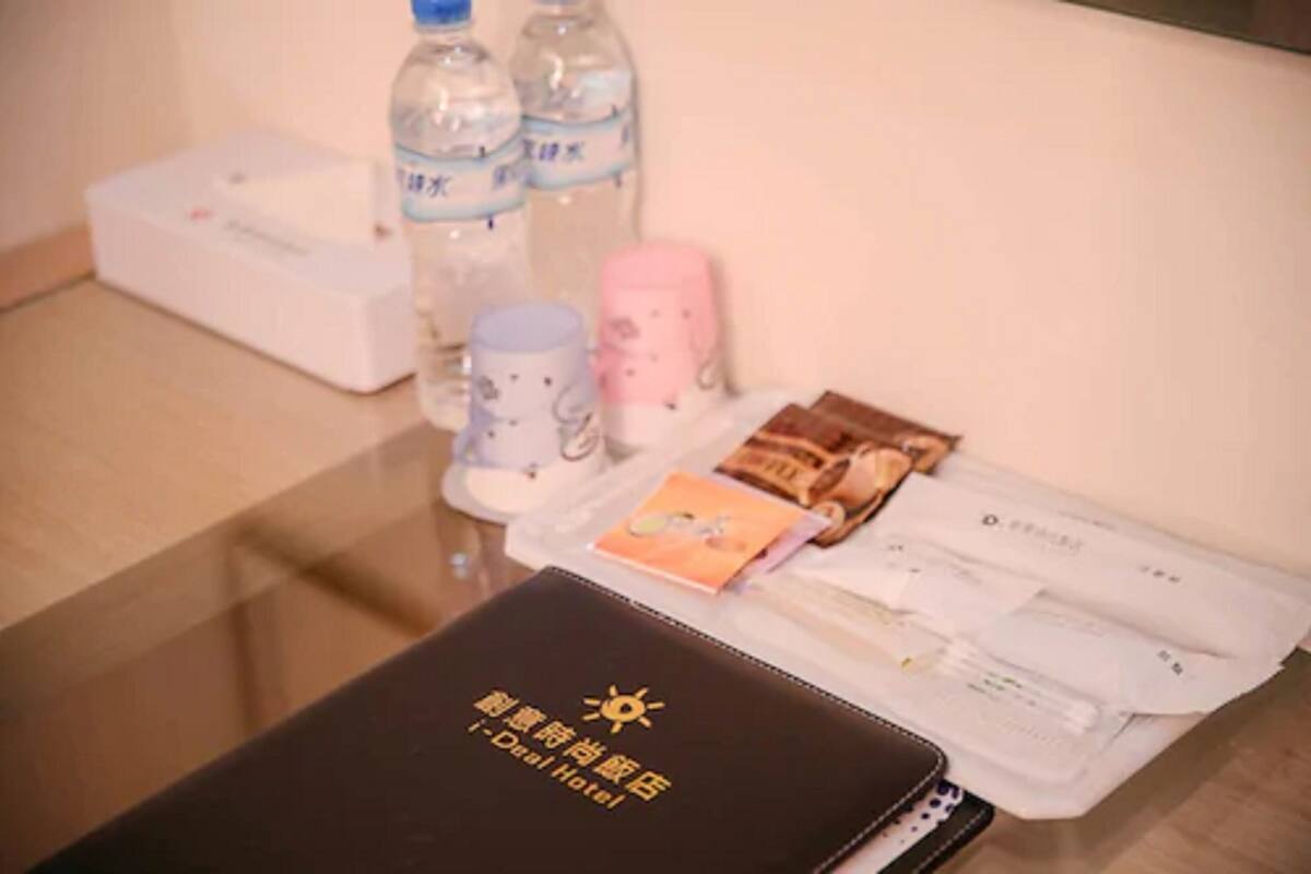 A table with a black folder labeled "i-Deal Hotel," a white box, two water bottles, a pink cup, a white cup, and some food packets.