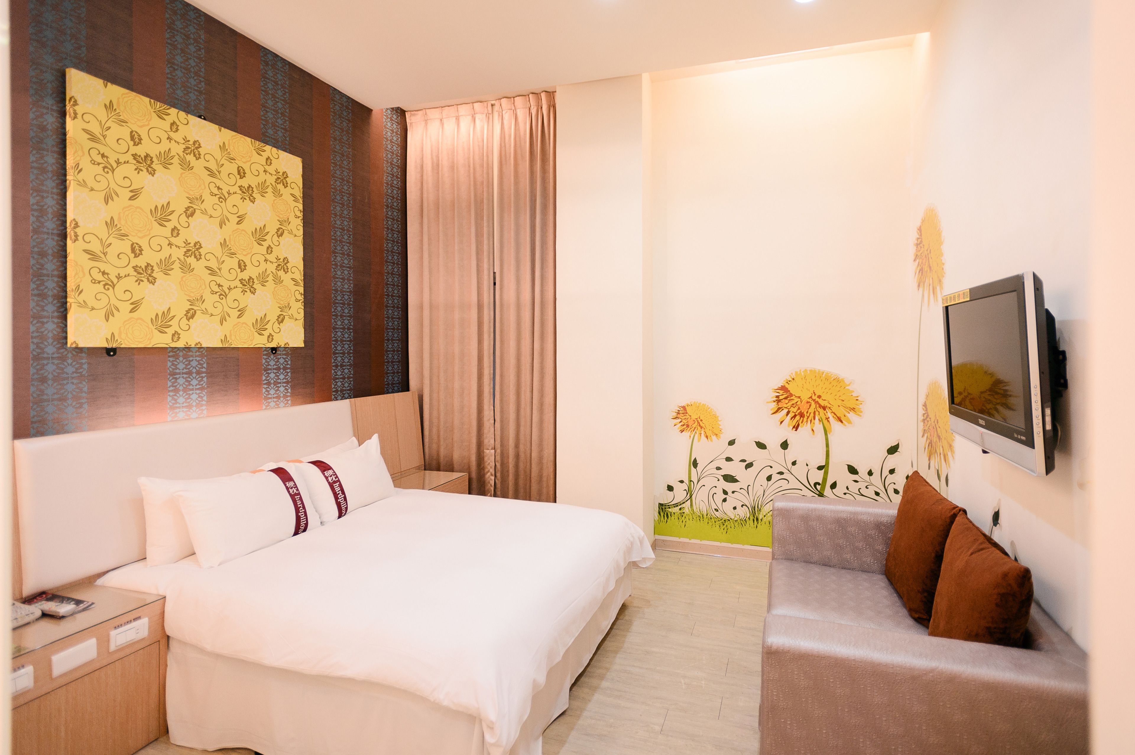 A hotel room with a bed, a sofa, a TV, a painting, and a window with curtains.