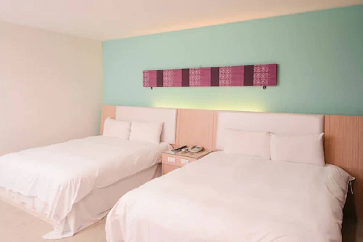 A hotel room with two beds, a wooden headboard, a nightstand, and a decorative wall piece.