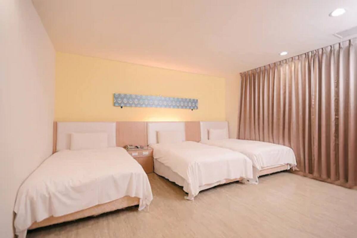 A hotel room with two single beds, a nightstand, a wall-mounted light fixture, and a curtain on the window.