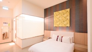 Una habitación de hotel con una cama grande, una mesita de noche con teléfono, una obra de arte en la pared y una puerta que da a un baño.