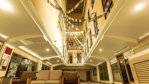 A spacious atrium with a high ceiling, a central staircase, and a seating area with wooden furniture.