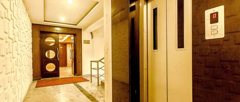 An interior corridor with an elevator, a door with a circular window, and a wall-mounted control panel.