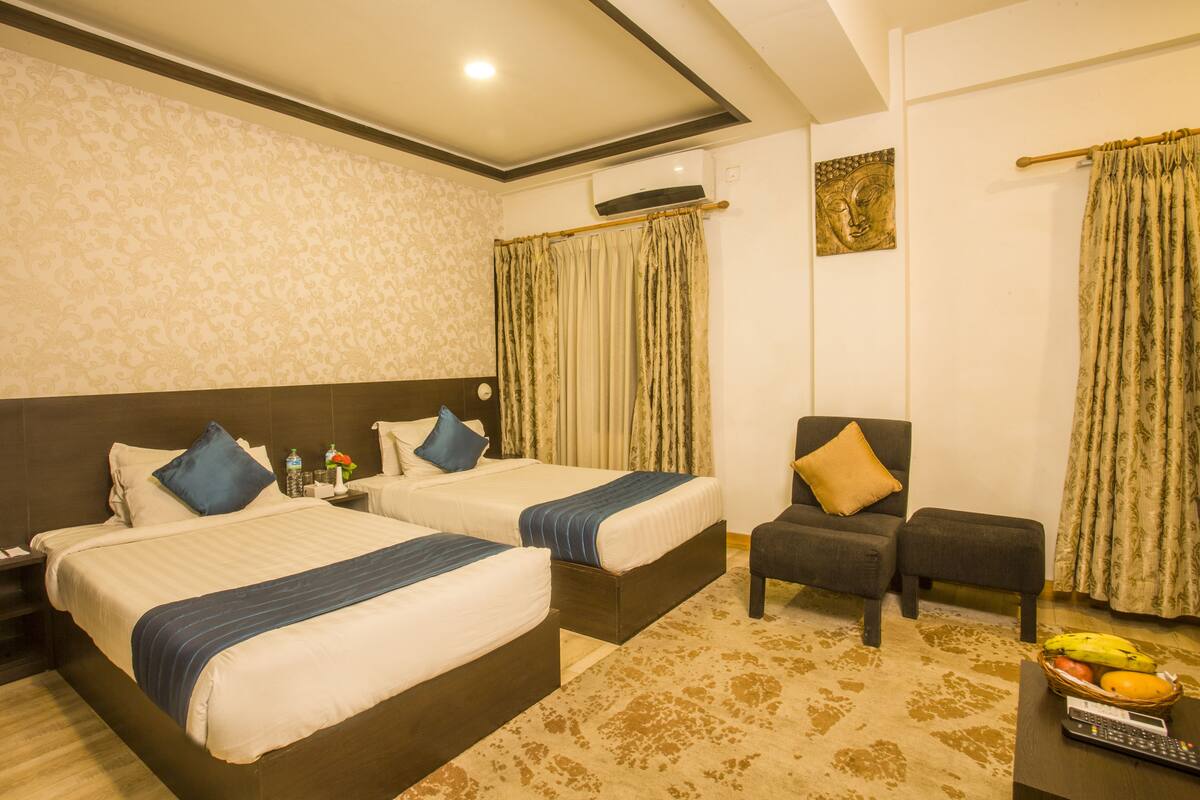 A hotel room with two beds, a sofa, a small table with fruits, and a decorative wall.