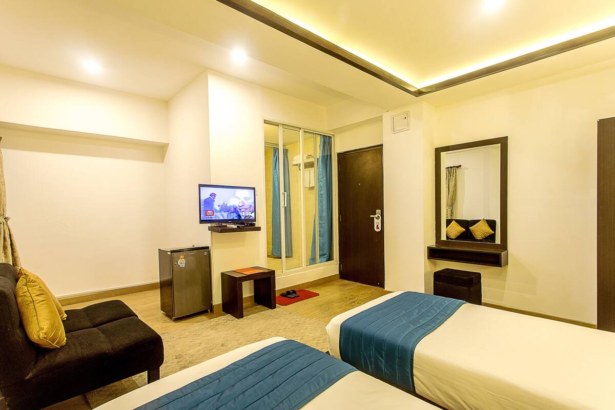 A hotel room with two beds, a TV, a desk, a mirror, and a sliding door to a bathroom.