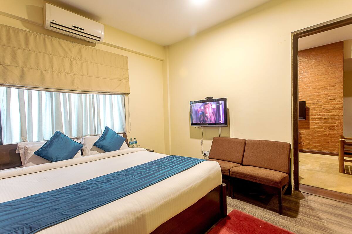 A hotel room with a bed, a TV, a sofa, and a red rug.