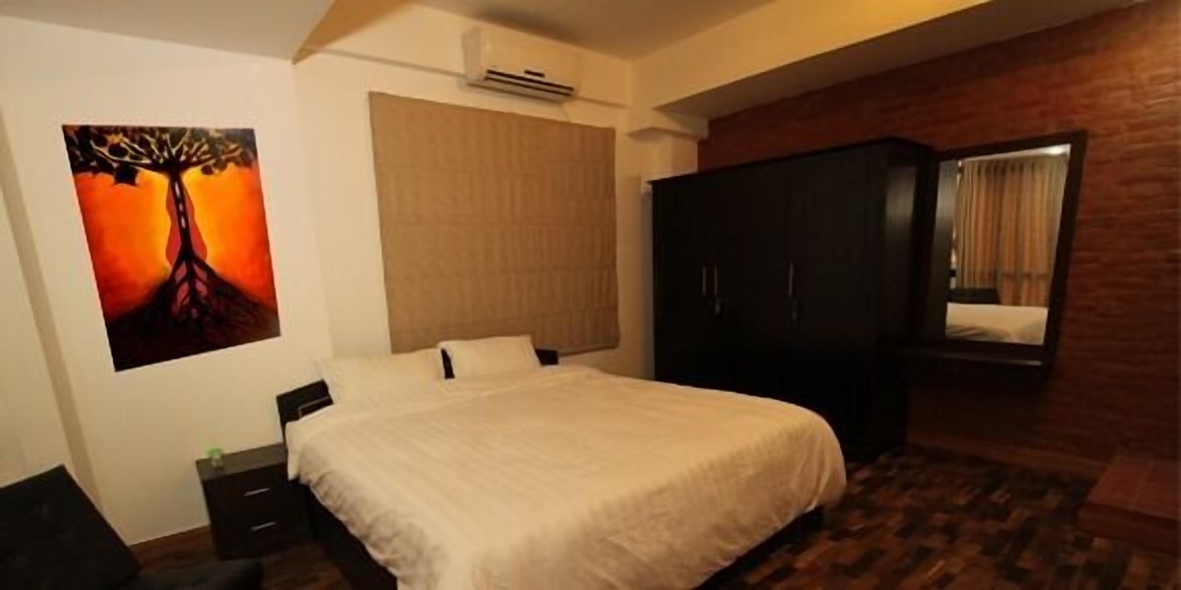 A bedroom with a bed, a wardrobe, a painting, and a window with curtains.