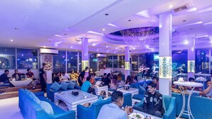 A modern lounge area with seating and tables, large windows, and decorative lighting.