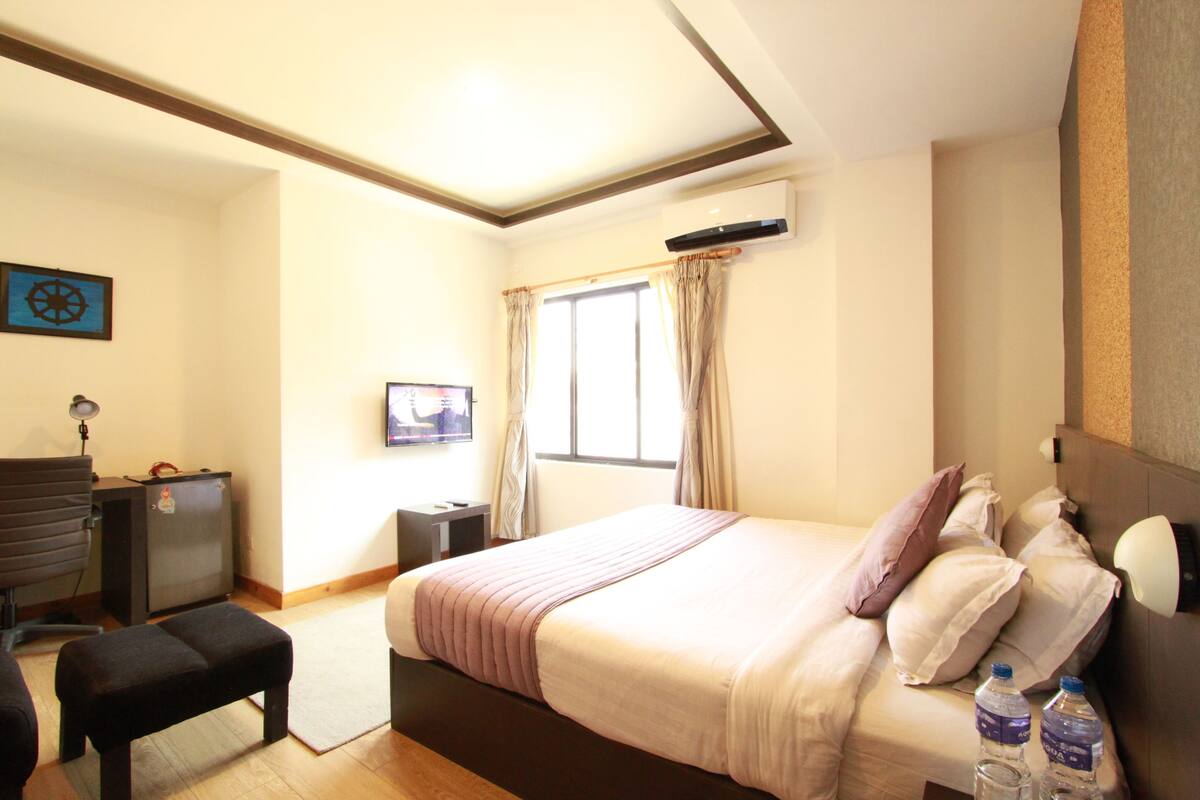 A hotel room with a bed, a desk, a chair, a television, and a window with curtains.