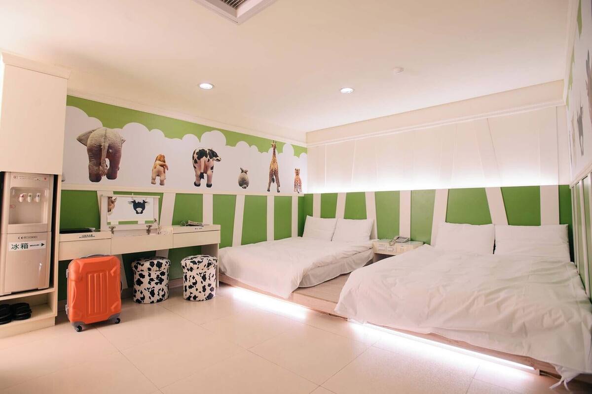 A hotel room with two beds, a desk, a chair, a wardrobe, and a wall with animal decals.