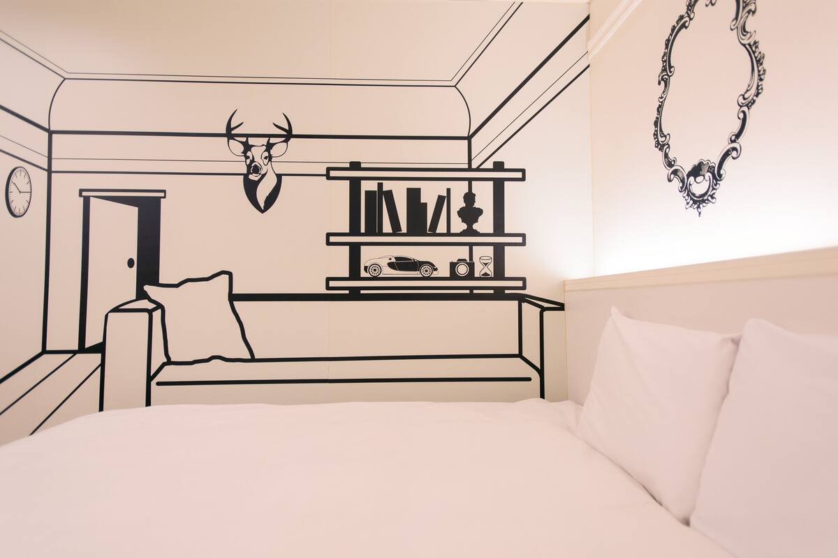 A bedroom with a bed, a nightstand, a shelf with books and a car model, a deer head decoration, and a necklace on the wall.