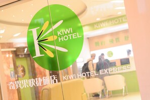 Logotipo circular verde con el texto "KIWI HOTEL" en un ventanal.