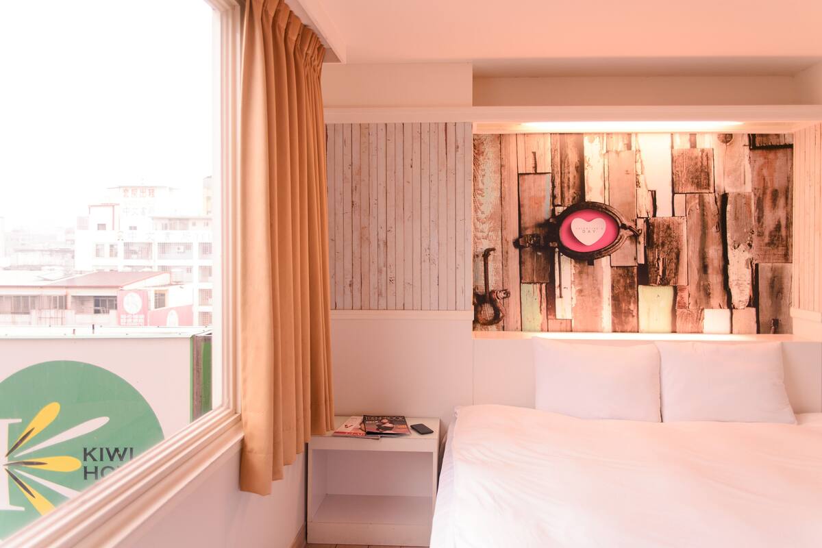 A hotel room with a bed, a nightstand, a wall-mounted clock, and a window with curtains.