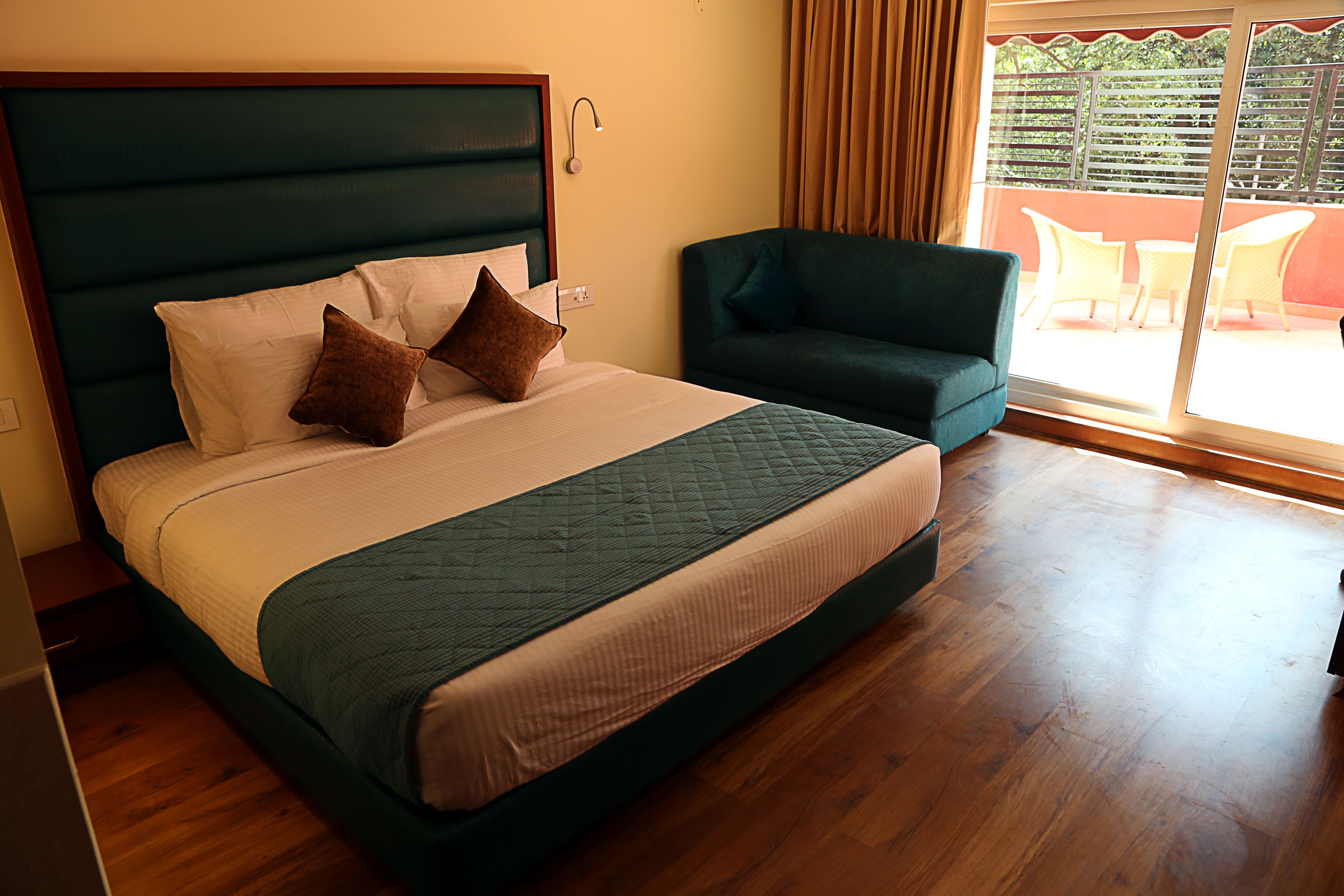 Una habitación de hotel con una cama grande, un sofá verde y un balcón con mobiliario exterior.