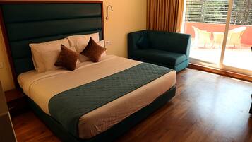 Una habitación de hotel con una cama grande, un sofá verde y un balcón con mobiliario exterior.