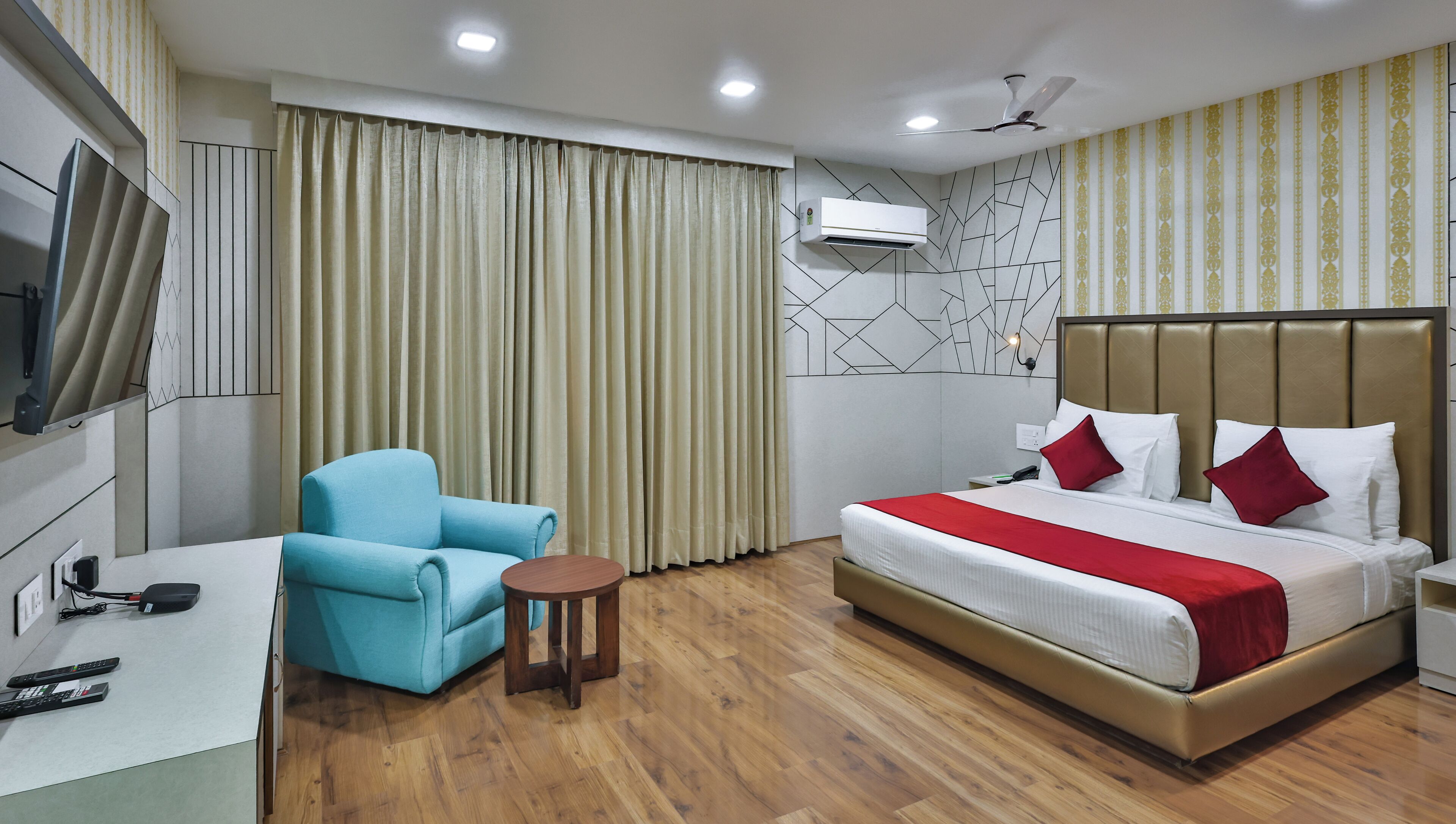 Quarto de hotel com cama, uma cadeira, uma mesinha, secretária com telefone e ar condicionado.