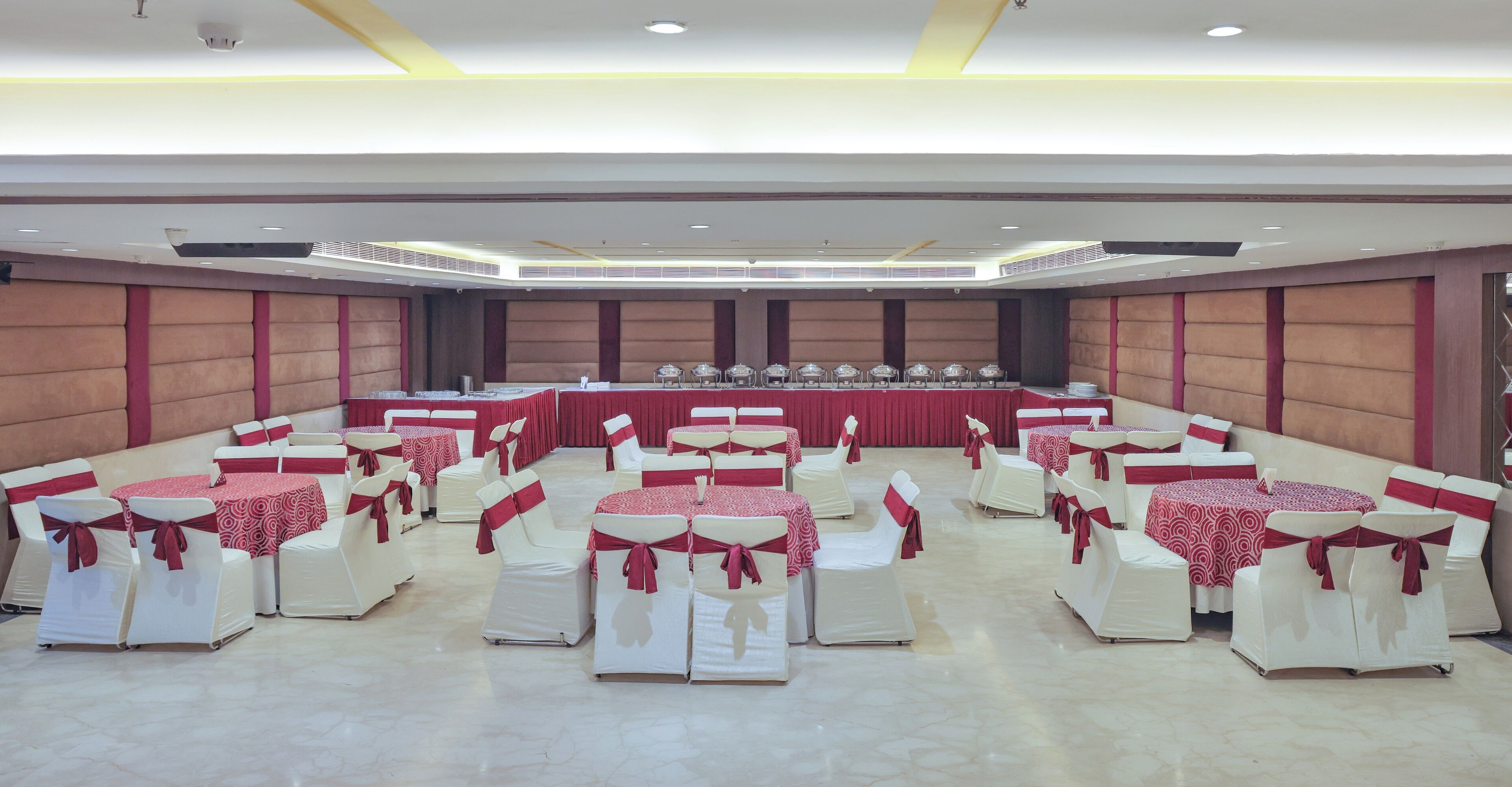 A banquet hall with rows of tables and chairs, a stage with a table, and a high ceiling with recessed lighting.