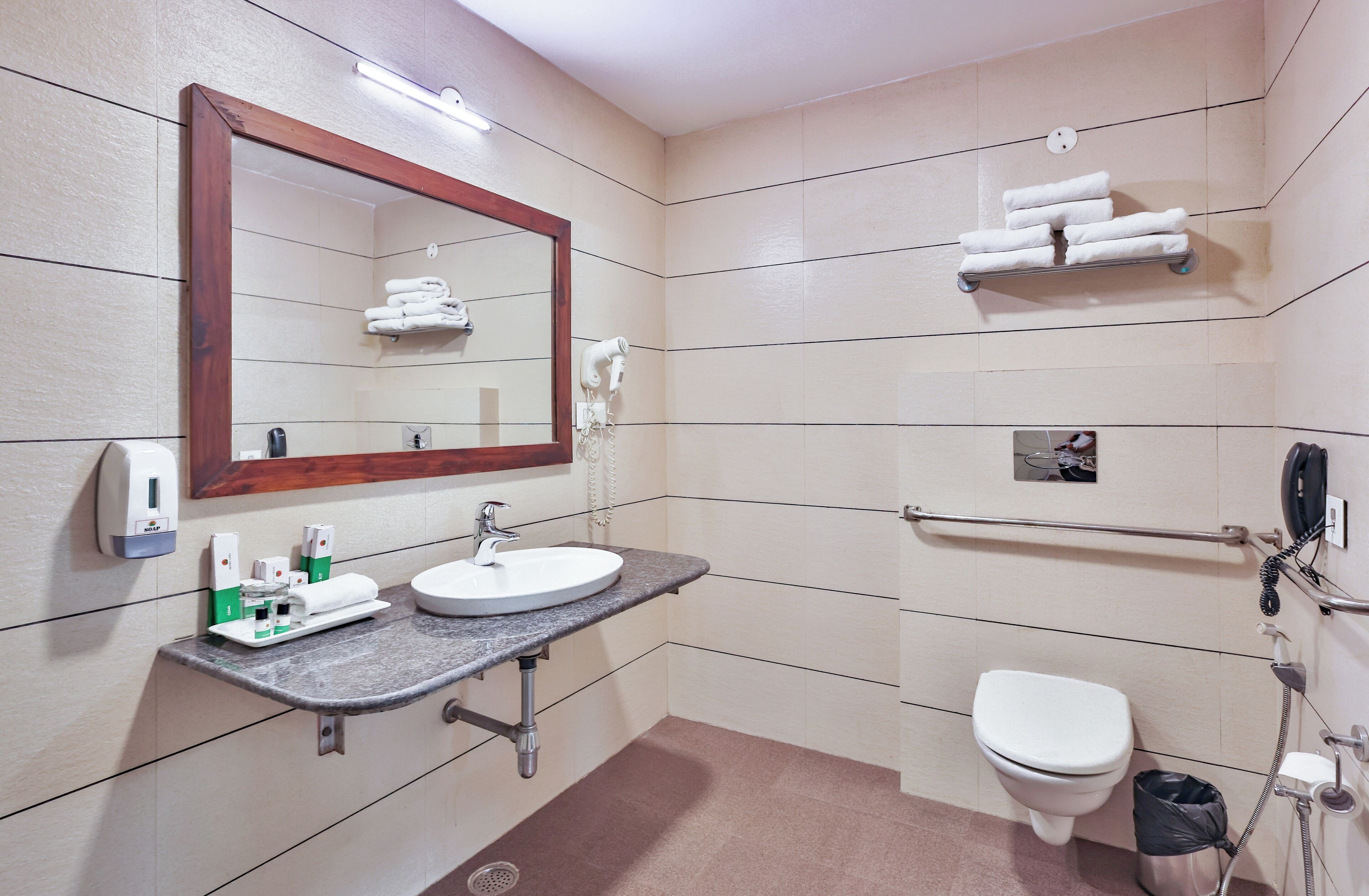 A bathroom with a sink, mirror, towel rack, toilet, and hand sanitizer dispenser.