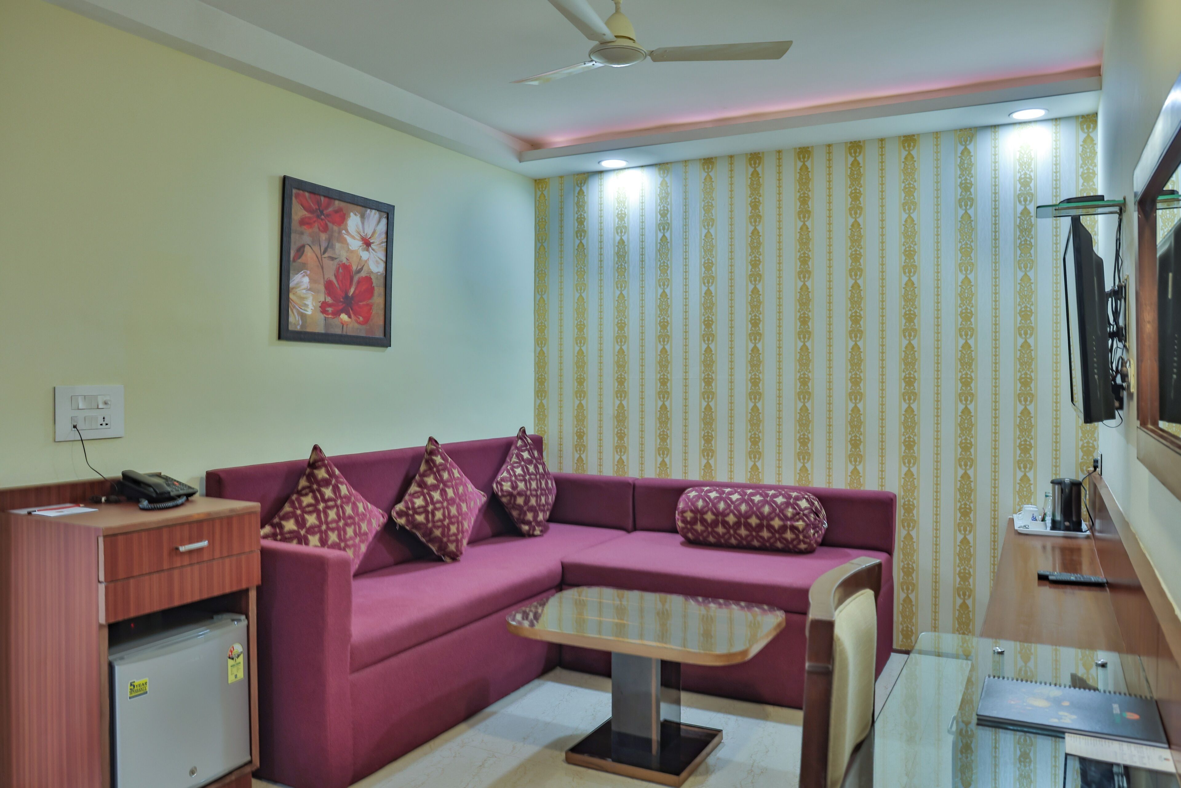 A living room with a purple sofa, a glass coffee table, a wooden desk, and a ceiling fan.
