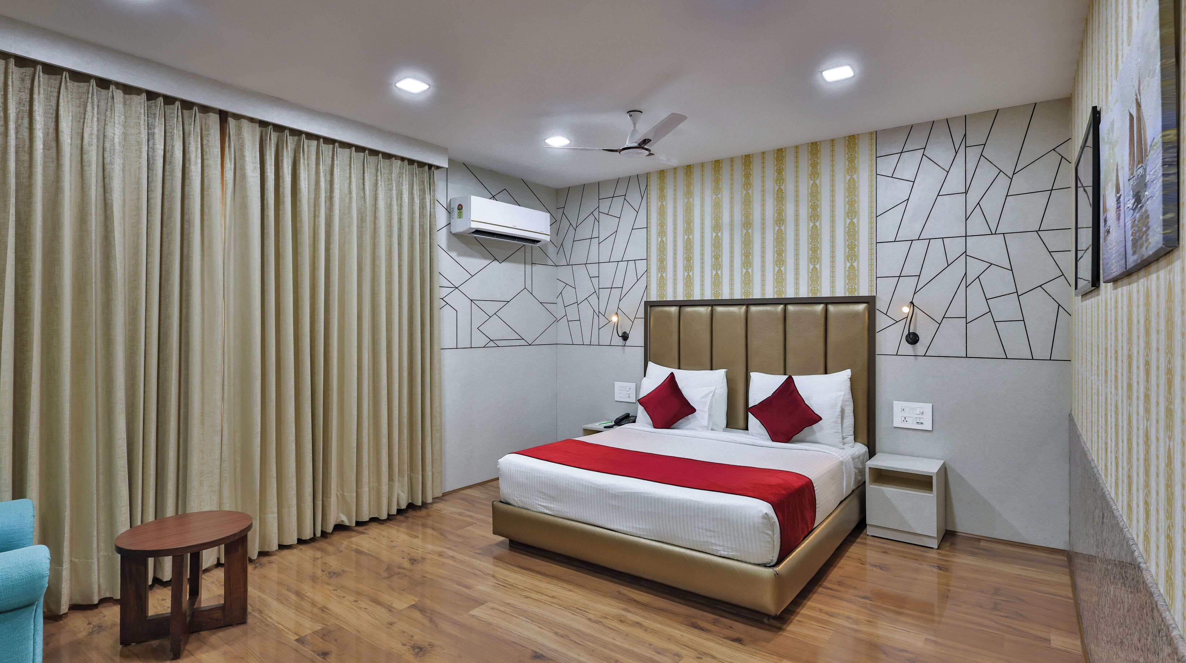 A hotel room with a bed, a nightstand, a small table, a ceiling fan, and a wall-mounted air conditioner.