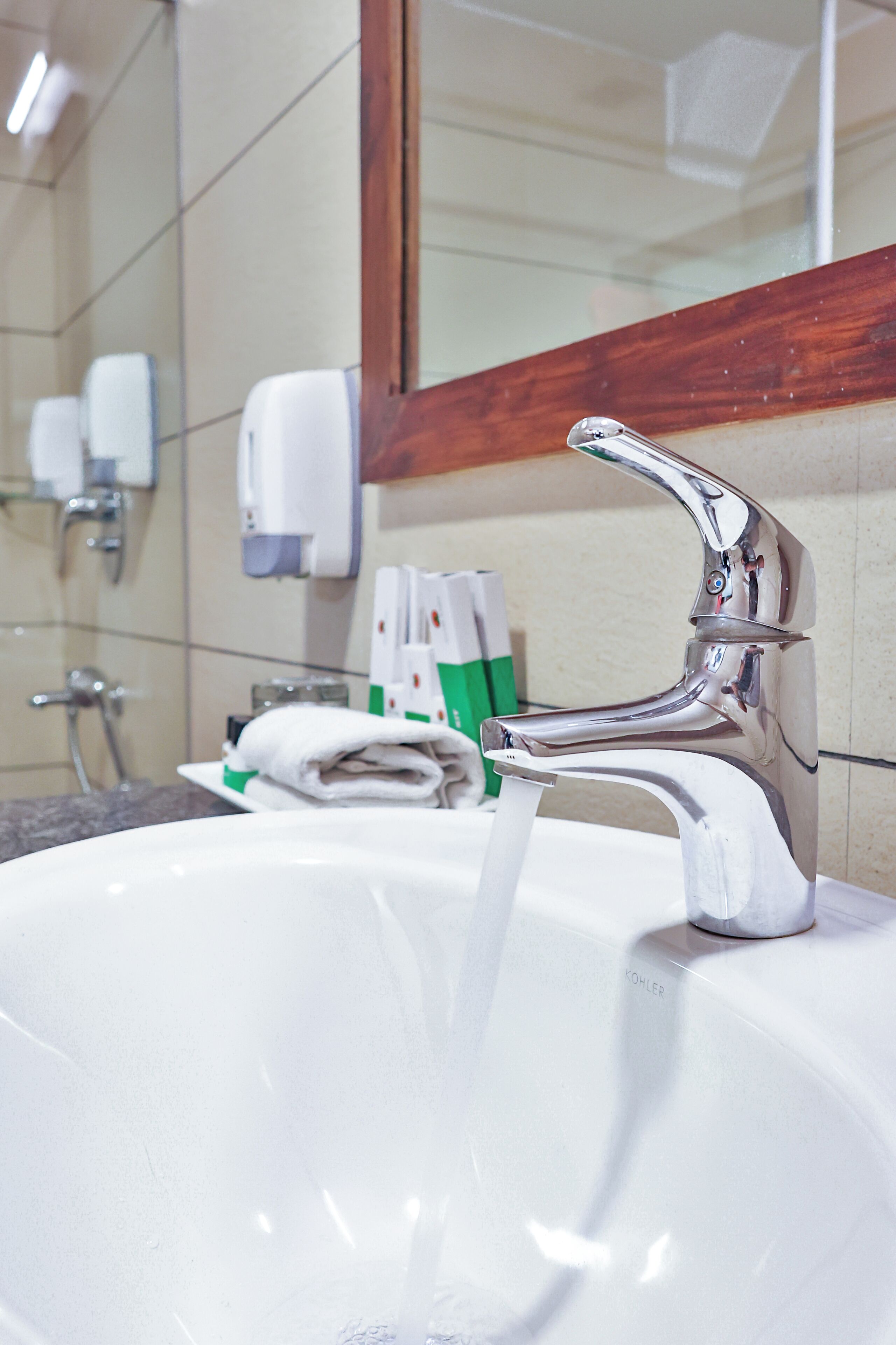 A bathroom sink with running water, a mirror, and soap dispensers.