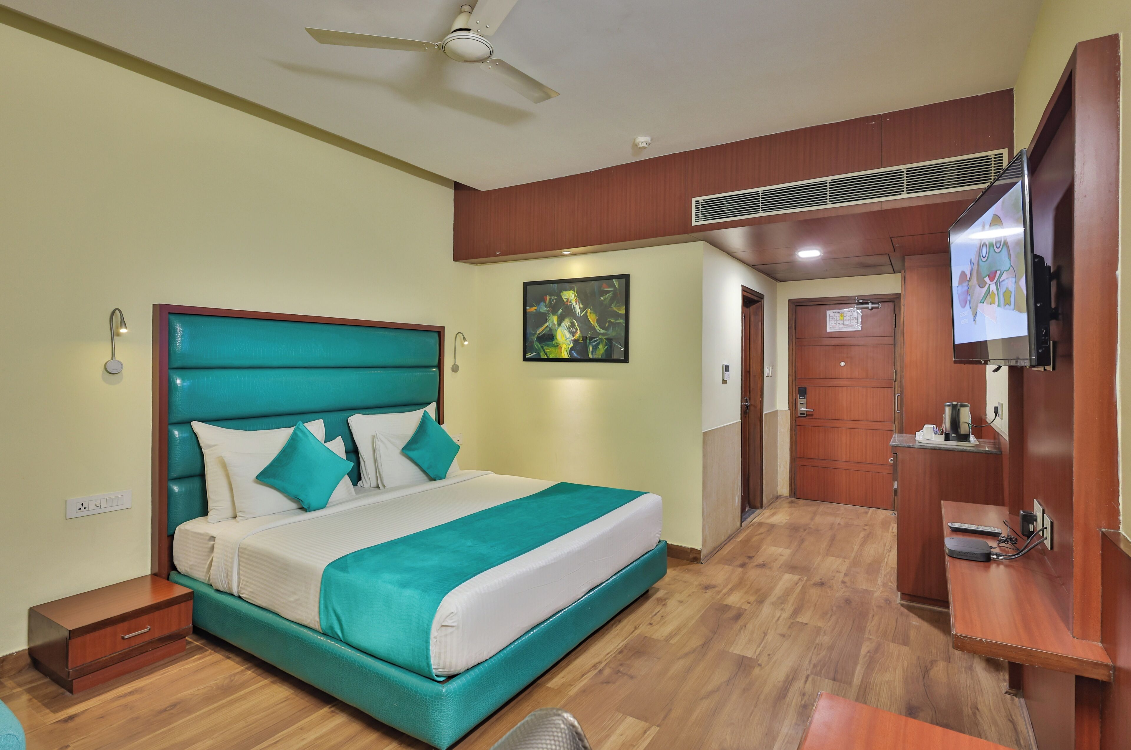 A hotel room with a large bed, a desk, a television, and a ceiling fan.
