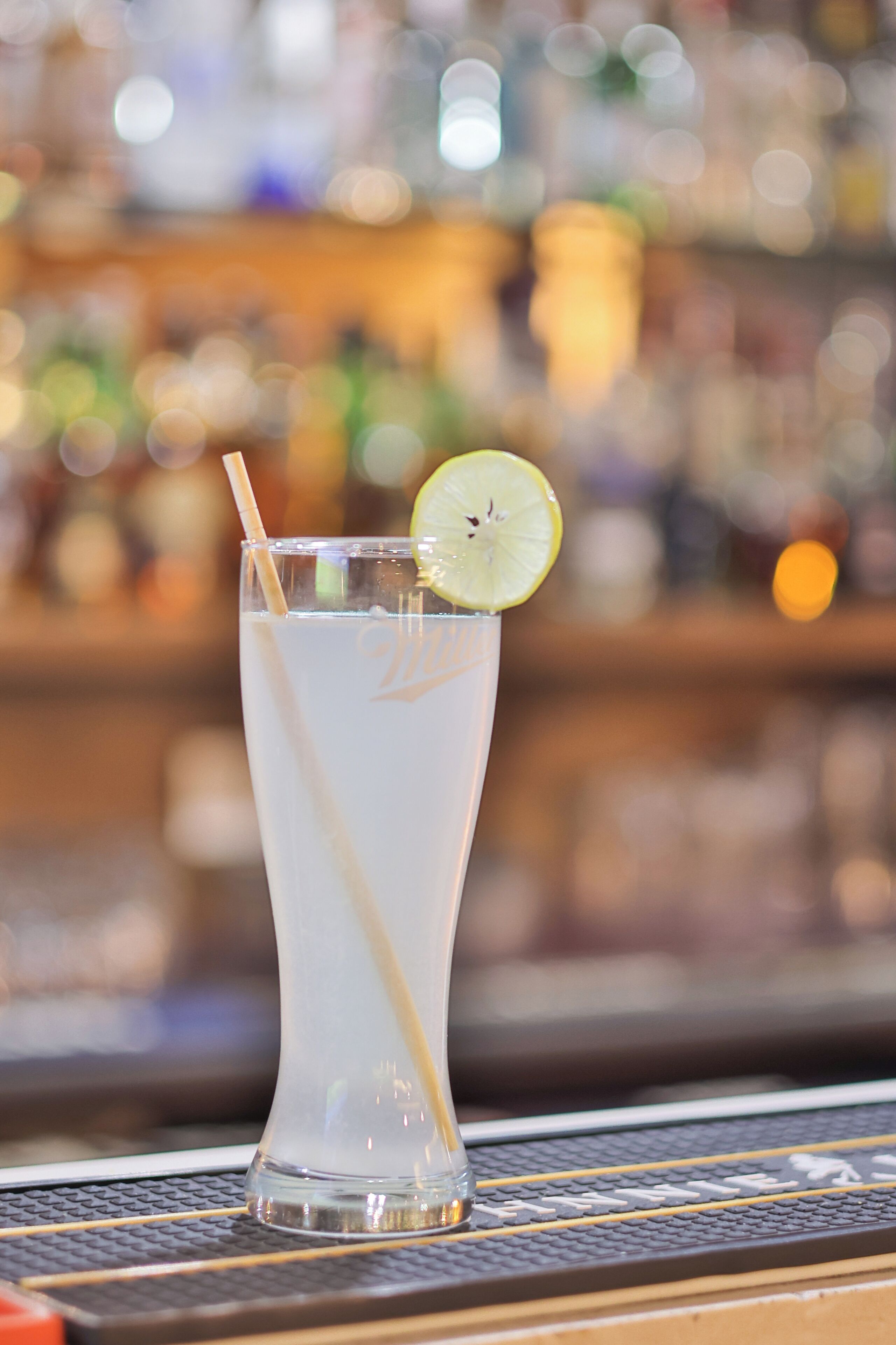 A clear glass with a straw and a lime slice on a bar counter.
